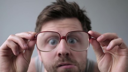 Wall Mural - Young man looking through huge glasses in shock with surprise expression.