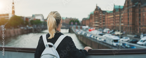 Cuadros en Lienzo Panoramic rear view of adult woman tourist with backpack enjoying historic wareh