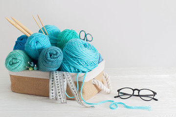  Blue and aquamarin yarn for knitting in a basket. Knitting needles, tape measure, glasses.