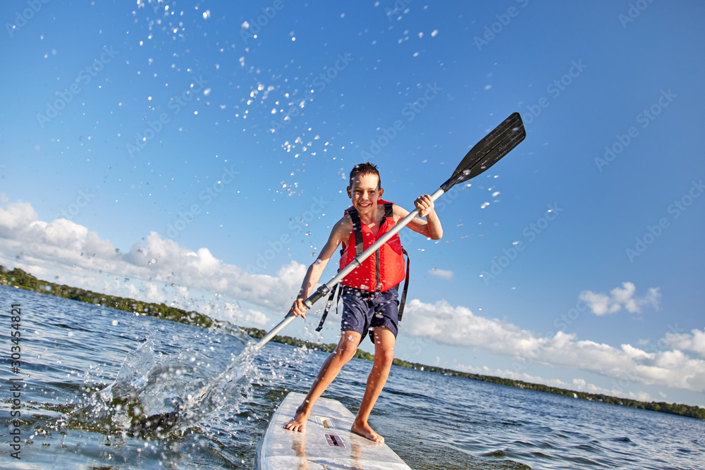 happy boy paddling on stand up paddleboard. cheerful child having fun on water. Summer vacation leisure activity, SUP boarding - obrazy, fototapety, plakaty 