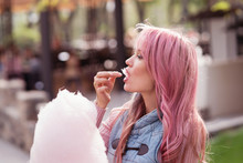 Adorable Young Woman With Long Pink Hair Eats And Poses With Sugar Pink Candy Cotton. Concept Happy Times. Carefree Girl. Good Mood