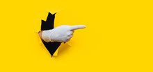 The Forefinger Points In White Medical Glove To The Right Side. Yellow Paper Background With Torn Hole. Place For Advertising. Copy Space.