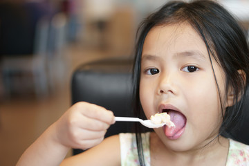 Wall Mural - Asian child cute or kid girl enjoy eating tuna salad and corn vegetable with yogurt for delicious breakfast and healthy food in morning with holding plastic spoon at home or restaurant and coffee shop