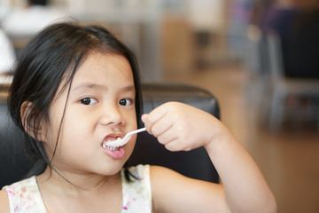 Wall Mural - Asian child cute appetite or kid girl enjoy eating tuna salad and corn vegetable or yogurt for breakfast and healthy food in morning with holding plastic spoon by left hand at home or cafe restaurant