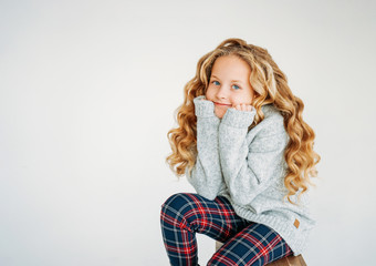 Beauty fashion portrait of smiling curly hair tween girl in cozy knitted sweater and plaid pants on white background isolated