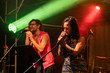 woman and man are singing and on the stage, male and female two singers performing during live music performance, blurred lights in the background
