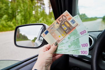 Euro banknotes of various denominations in a woman hand inside of a car