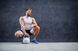 Caucasian sporty muscular man posing, crouching and holding kettle bell outdoors.