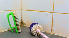 Close Up Dirty Green Toilet Brush With Plastic Handle On Restroom Floor Over The Dirty Ceramic Wall. Dirty Bathroom And Toilet Floor Cleaning Concept.