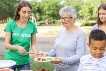 Wall Mural - Young volunteer giving food to poor people outdoors