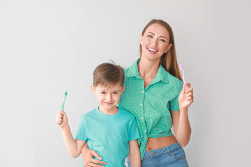 Wall Mural - Portrait of mother and her little son brushing teeth on light background