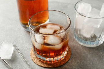 Bottle, glasses with ice cubes and whiskey on grey background, close up