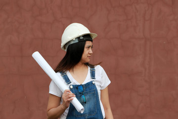 Female civil engineer or architect with white helmet and project drafts while in hand standing on brown background.