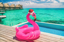 Christmas Summer Vacation Pool Float Pink Flamingo Wearing Santa Hat Travel Background Winter Holidays. Traveling South To Enjoy Sun And Heat At Luxury Resort Overwater Bunglaows In Bora Bora, Tahiti.