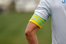 Captain Of The Football Team On The Stadium Field. Sports Background-the Hand Of The Team Captain With The Identifying Distinctive Ribbon Of The Captain, Official Leader Of Team Of Footballers
