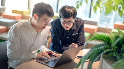 Business meeting and partnership concept. Asian man colleagues discussing about startup project using laptop computer and digital tablet in office. Coworkers team sharing ideas together at workplace.