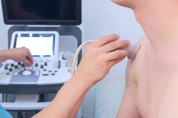 Wall Mural - Doctor makes ultrasound of shoulder joint to man using ultrasound scanner in clinic, closeup. He runs ultrasound sensor over man's arm, working on scanner panel and looking at screen.