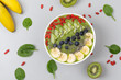 Healthy breakfast smoothie bowl topped with blueberry, kiwi, banana, spinach, Chia seeds and Goji berries. Detox concept. Green smoothie bowl on grey background. Top view.