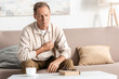 © LIGHTFIELD STUDIOS - sick retired man touching chest while sitting on sofa