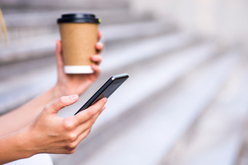 Woman hold cup of coffee and smart phone on street, with space for text.