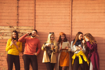 group of young people millennials using smart phones and tablets, calling, searching web, smiling, taking selfies, outdoor autumn poster ready  beautiful boy and girls