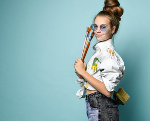 Cheerful smiling young woman in white shirt with paint stains with a set of brushes and one in back pocket of her jeans