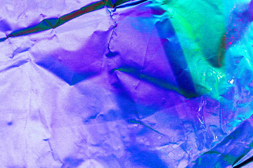 Texture of crumpled aluminum kitchen foil with reflected purple and green light. Colorful abstract background for design.