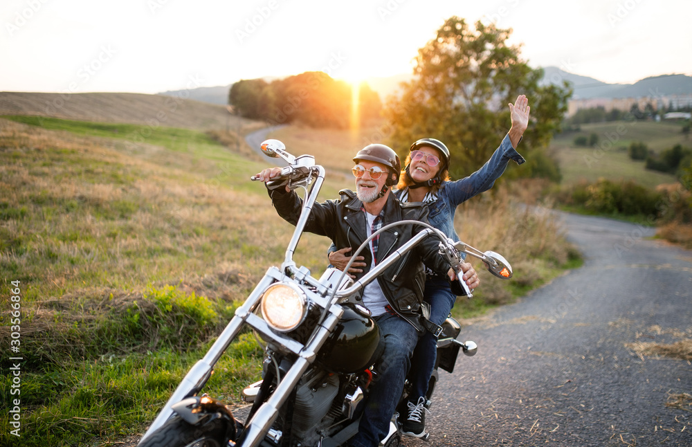 A cheerful senior couple travellers with motorbike in countryside. - obrazy, fototapety, plakaty 