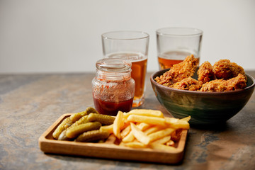 Wall Mural - delicious chicken nuggets, french fries and gherkins near glasses of beer on stone surface isolated on grey