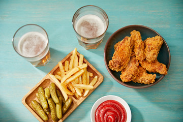 Wall Mural - top view of delicious chicken nuggets, ketchup, french fries and gherkins near glasses of beer on turquoise wooden table