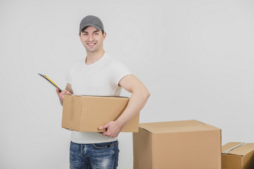 Handsome young delivery man standing with clipboard and carton box in his hands, looking at the camera, smiling.