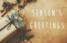Season's Greetings Text Sign On Stylish Rustic Christmas Gifts Box With Cedar Branch On Rural Table With Pine Cones, Gingerbread Cookies, Cotton, Cinnamon. Season's Greeting Card