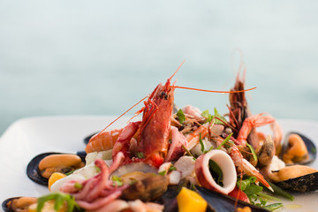 Canvas Print - Mixed seafood salad (shrimps, mussels, squids) on the table, located on the beach. Ischia, Italy.