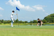 © freebird7977 - Group Professional Golfer asian man and friend playing aiming shot for putting ball on the hole with club on green course.  Hobby in holiday and vacations in sunny morning on multiethnic club golf.