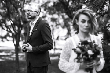 Beautiful black and white photo of bride and groom. Happy couple posing and smiling in wedding dress and suit with bridal bouquet in the park. People enjoy each other.  Together. Wedding concept.