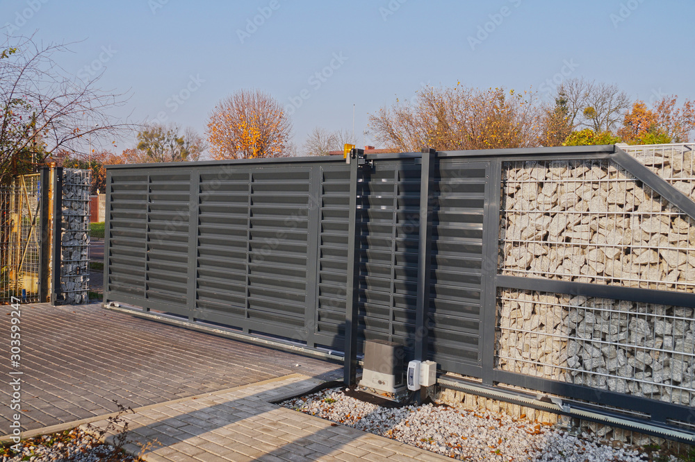Gabion. Automatic entrance gate used in combination with a wall made of gabion. - obrazy, fototapety, plakaty 