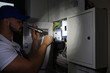 © New Africa - Electrician with flashlight fixing electric panel indoors