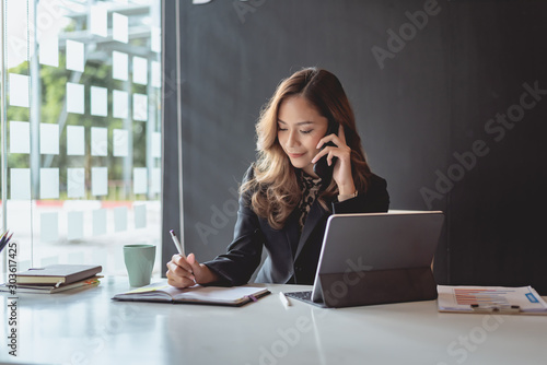 Fotografía Young asian businesswoman beautiful charming smiling and talking on the mobile phone in the office