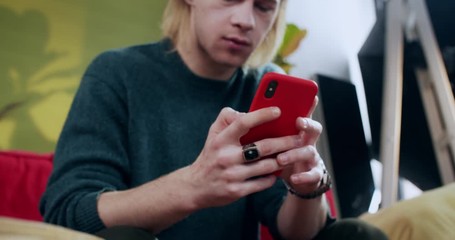 Young blonde man browsing smartphone internet news content texting message resting at home. Close-up. Casual people. Mobile addiction.