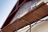 Fototapeta Zwierzęta - Scaffolding around house with beige siding covering walls. Construction site.