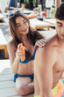cheerful young woman applying sunscreen lotion on boyfriends shoulder
