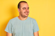 © Krakenimages.com - Young man wearing green casual t-shirt standing over isolated yellow background looking away to side with smile on face, natural expression. Laughing confident.