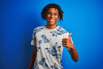 Wall Mural - Afro american man with dreadlocks wearing summer floral t-shirt over isolated blue background doing happy thumbs up gesture with hand. Approving expression looking at the camera with showing success.
