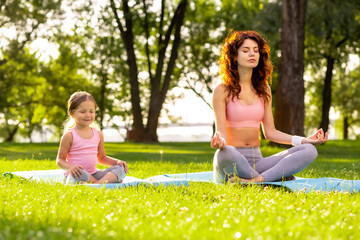 Wall Mural - mother and daughter with closed eyes sitting in lotus positing together in the park