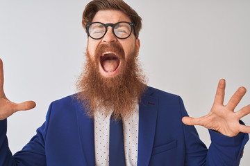 Sticker - Young redhead irish businessman wearing suit and glasses over isolated white background celebrating mad and crazy for success with arms raised and closed eyes screaming excited. Winner concept