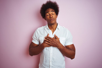 Sticker - Young american man with afro hair wearing white shirt standing over isolated pink background smiling with hands on chest with closed eyes and grateful gesture on face. Health concept.