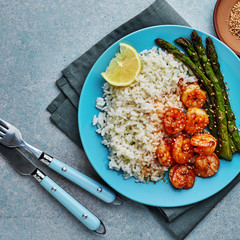 Wall Mural - Delicious teriyaki coated shrimps stir fry with grilled asparagus, rice and sesame on a blue plate. Healthy seafood meal. Top view, directly above shot.