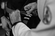 Promotion during brazilian jiu jitsu training. Close up, black and white photo of trainer's hand adding third white stripe to adept's belt.