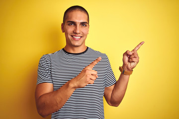 Poster - Young handsome man wearing striped t-shirt over yellow isolated background smiling and looking at the camera pointing with two hands and fingers to the side.