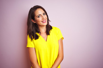 Wall Mural - Young beautiful woman wearing yellow t-shirt standing over pink isolated background looking away to side with smile on face, natural expression. Laughing confident.